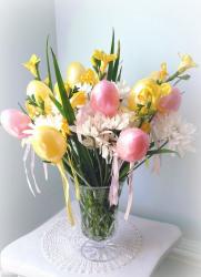 Cute Easter table arrangement with white and yellow spring flowers with pink easter eggs and yellow easter eggs